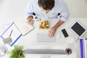 Overhead View Of Businessman Working At Computer In Office Eating Lunch